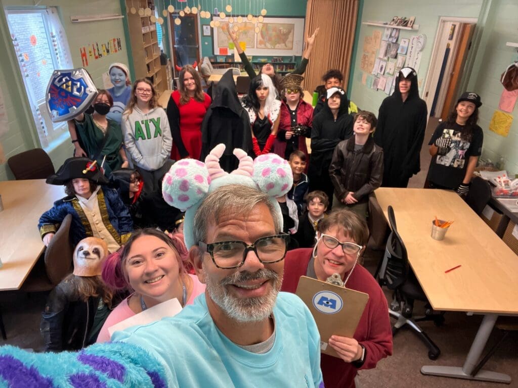 Teacher takes selfie with middle schoolers dressed in halloween costumes at private school.