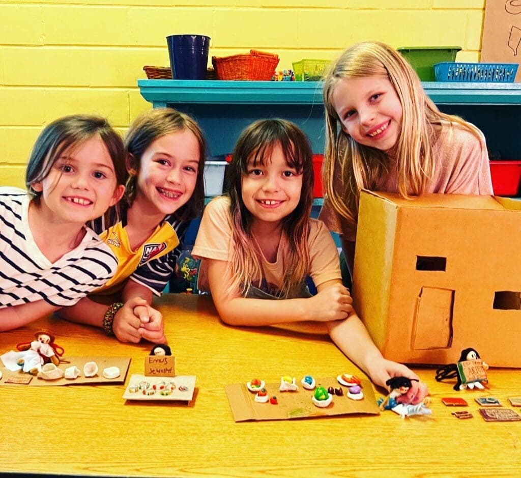 Four third grade girls smile as they present their project at part time school.