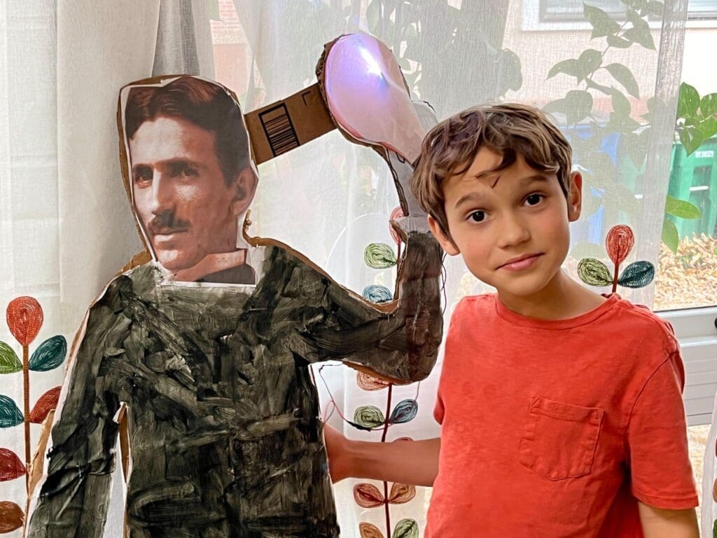 Student stands beside life sized cut out of Tesla at project based school.