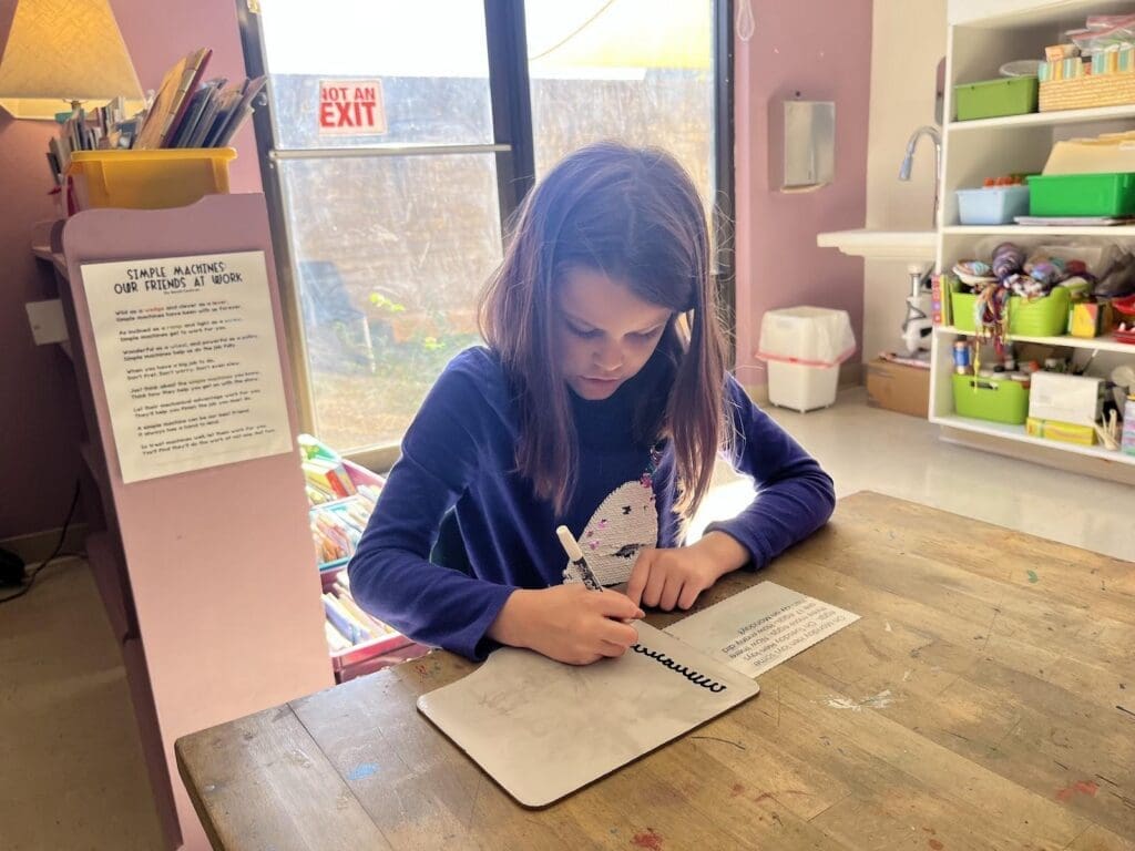 Elementary student works at table in well lit room at micro school.