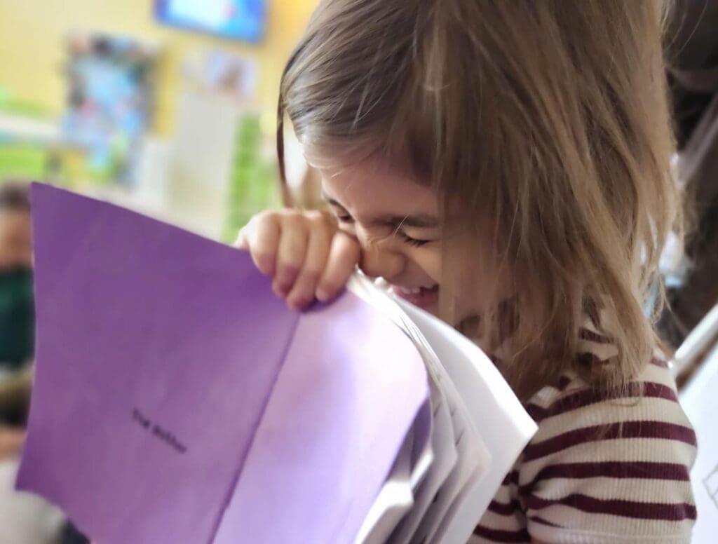 Kindergartener laughs while holding notebook at school with small classes.