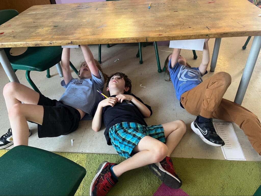 Three elementary students work under table at project based school.