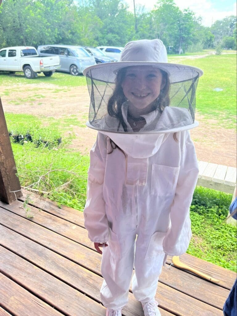 Elementary student wears beekeeper outfit at experiential school.