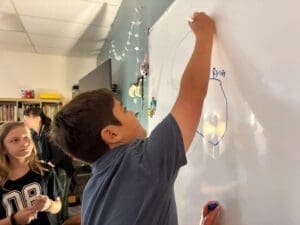 Middle school student works at white board at school with small class sizes.