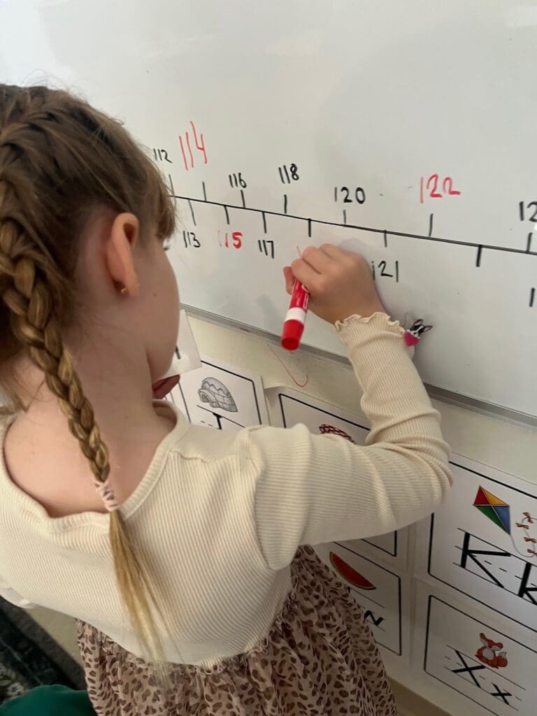 Elementary student writes on white board at school with small class sizes.