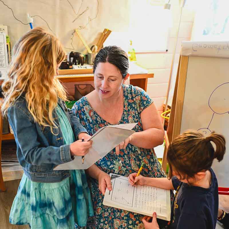 Kindergarten teacher assists two students with math work.